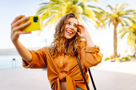 Tourist takes selfie with smartphone camera while walking along sunny streets of resort town.の写真素材