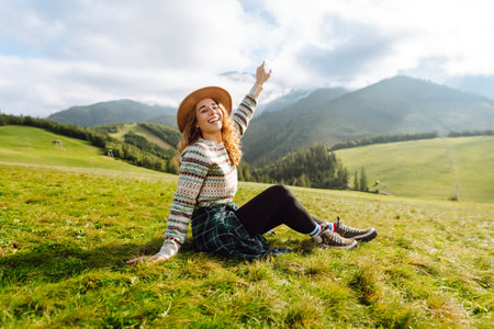 Stylish female traveler in hat has fun on top of hill, enjoys mountain landscape. Active lifestyle.の写真素材