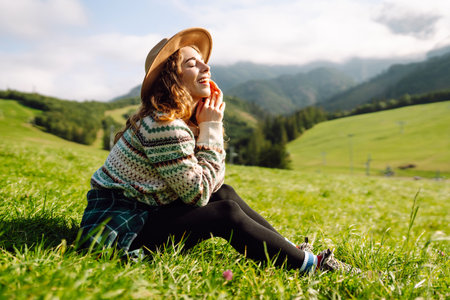 Stylish female traveler in hat has fun on top of hill, enjoys mountain landscape. Active lifestyle.の写真素材