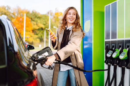 Beautiful woman filling car with gasoline at gas station. Online pay. Woman using app on phone.の写真素材