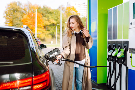 Beautiful woman filling car with gasoline at gas station. Online pay. Woman using app on phone.の写真素材