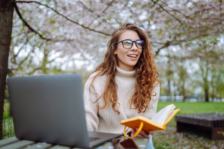 Beautiful female student is using laptop, notepad to prepare for outdoor classes. Education concept.の写真素材