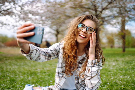 Young woman takes selfie against background of flowering trees in park. Concept of relaxation, fun.の写真素材