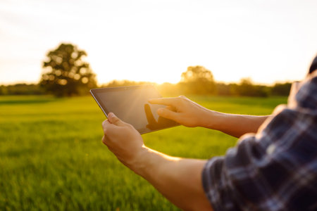 Close-up of the hands of farmer with digital tablet, checking the quality of wheat growth in green fieldの写真素材