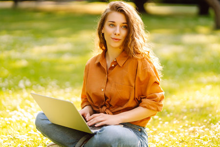 Portrait of a happy woman in sunny park on green lawn with a laptop. Freelance concept, technology.の写真素材