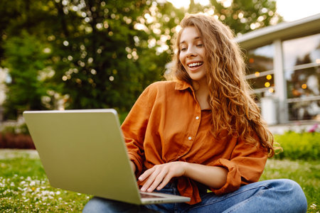 Portrait of a happy woman in sunny park on green lawn with a laptop. Freelance concept, technology.の写真素材