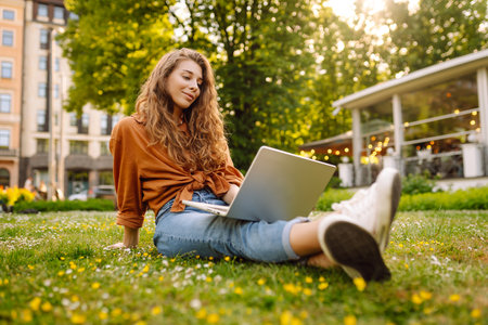 Portrait of a happy woman in sunny park on green lawn with a laptop. Freelance concept, technology.の写真素材