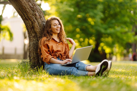 Portrait of a happy woman in sunny park on green lawn with a laptop. Freelance concept, technology.の写真素材