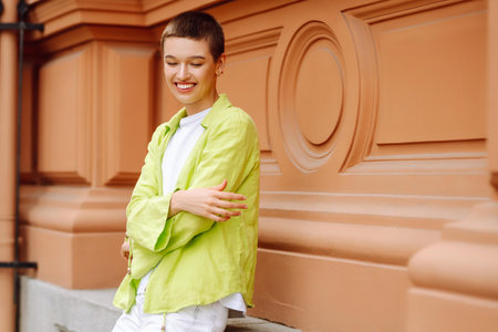 Positive woman with a short haircut and a green shirt walks and relaxes on the streets of the city.の写真素材