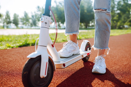 Woman riding electric kick scooter outdoors at sunset, closeup. Ecological transportation concept.の写真素材