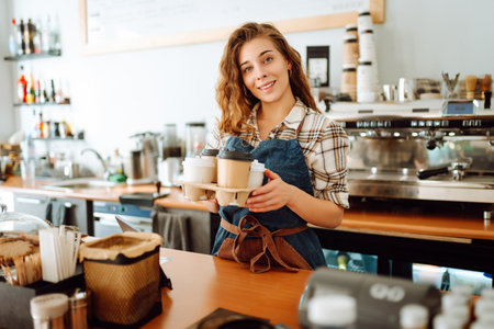 Portrait of a young female barista with a glass holder with drinks to go. Takeaway delivery concept.の写真素材