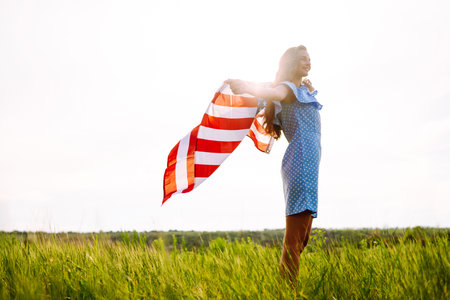 Young woman with American USA flag on blooming meadow. Independence Day, 4th July.の写真素材