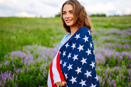 Young woman with American USA flag on blooming meadow. Independence Day, 4th July.の写真素材