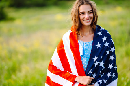 Young woman with American USA flag on blooming meadow. Independence Day, 4th July.の写真素材