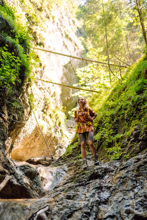 Woman traveler with a hiking yellow backpack explores new places, collects water from a streamの写真素材