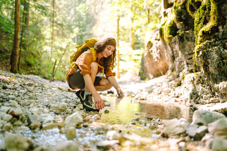 Woman traveler collects water from a stream, climbs up the mountains along a forest hiking trail.の写真素材
