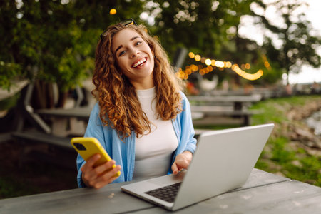 Cute woman in glasses with laptop and smartphone working outdoors. Technology, freelancing.の写真素材