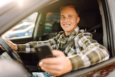 Smiling man using smartphone sitting on driver's seat in car. Car travel, lifestyle concept.の写真素材