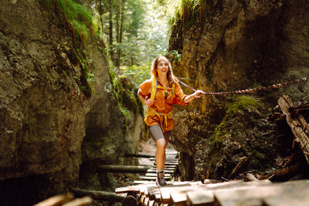 Happy woman in hiking clothes walks along wooden hiking path in mountains. Outdoor adventure conceptの写真素材