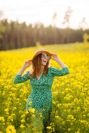 Beautiful woman in bright dress and elegant hat walks and has fun in rapeseed field. Nature, rest.の写真素材