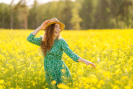 Beautiful woman in bright dress and elegant hat walks and has fun in rapeseed field. Nature, rest.の写真素材