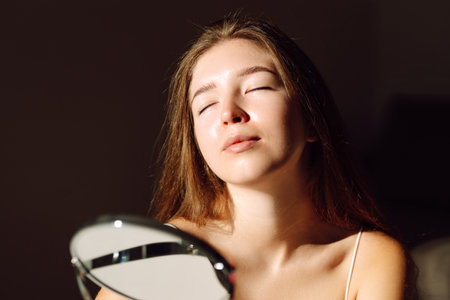 Cute woman with rashes on her face looks into small mirror. Natural skin without filter. Cosmetologyの写真素材