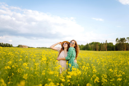 Two young women in beautiful dresses walk in a field with yellow blooming rapeseed. Concept of fun.の写真素材
