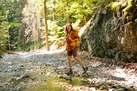 Woman traveler collects water from a stream, climbs up the mountains along a forest hiking trail.の写真素材