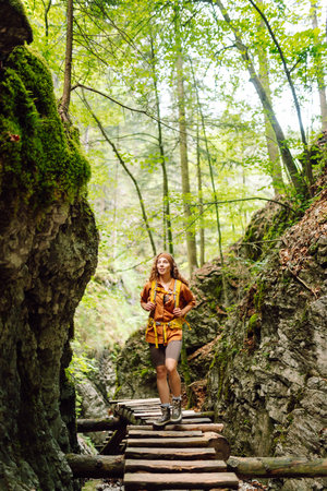 Happy woman in hiking clothes walks along wooden hiking path in mountains. Outdoor adventure conceptの写真素材