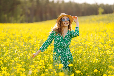 Beautiful woman in bright dress and elegant hat walks and has fun in rapeseed field. Nature, rest.の写真素材