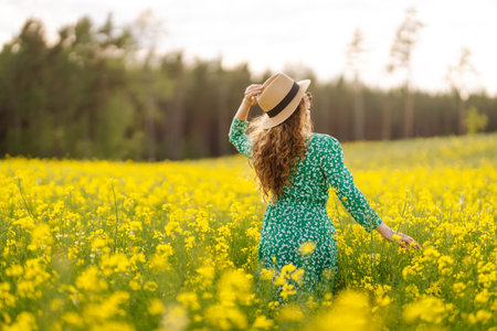Beautiful woman in bright dress and elegant hat walks and has fun in rapeseed field. Nature, rest.の写真素材