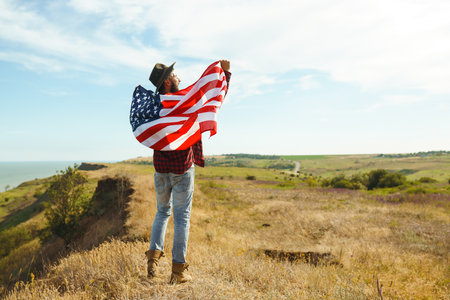 4th of July. American Flag. Traveler with the flag of America. The man in a hat, a backpack, a shirt and jeans.の写真素材