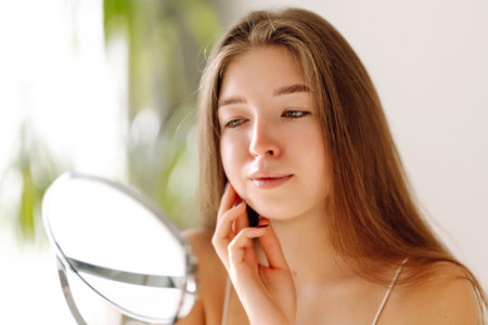 A beautiful woman looking in mirror, examines acne, pigmentation. Cosmetic care. Allergic reaction.の写真素材