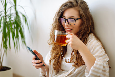 A young curly woman drinks coffee or tea while sitting on the floor in the living room.の写真素材