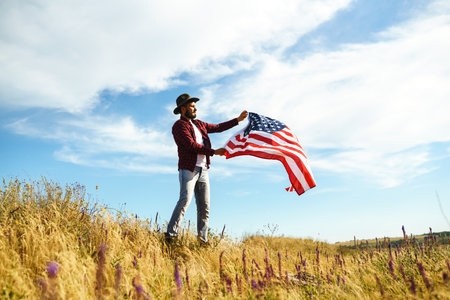 4th of July. American Flag. Traveler with the flag of America. The man in a hat, a backpack, a shirt and jeans.の写真素材