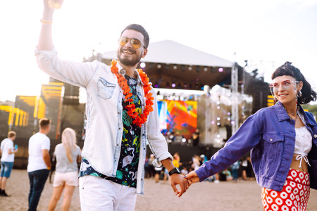 Young and cheerful couple at music festival. Happy friends drinking beer and having fun.の写真素材
