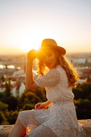 Smiling female tourist in hat admires landscape of city at dawn. Euro-trip. Active lifestyle conceptの写真素材