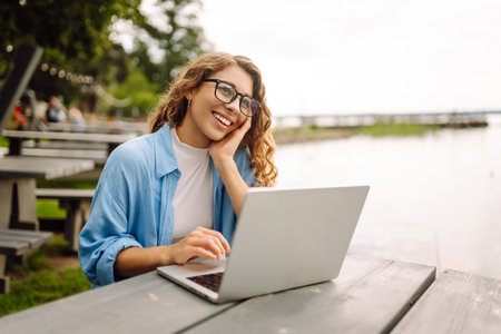 Portrait of woman in blue shirt with laptop at table in outdoor cafe near a lake. Freelance concept.の写真素材