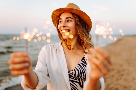 The sparklers in hands of young woman on the beach. Woman enjoying party on beach with sparklers.の写真素材