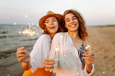 Beautiful Two women holding sparkler celebration on beach. They are having a great time together!の写真素材