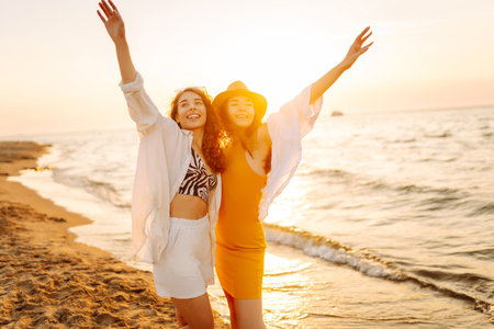 Portrait of two young female friends walking on the sea shore at sunset. Lifestyle concept.の写真素材