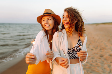 Beautiful Two women holding sparkler celebration on beach. They are having a great time together!の写真素材