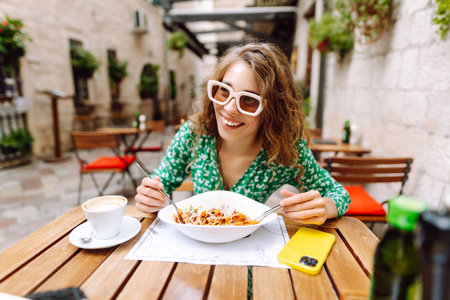 Young woman sitting in summer cafe, eating pasta with tomato, meat. Bolognese. Parmesan cheese.の写真素材
