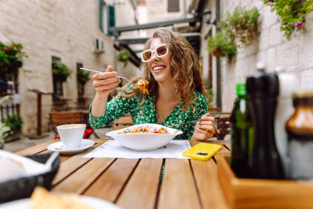 Young woman sitting in summer cafe, eating pasta with tomato, meat. Bolognese. Parmesan cheese.の写真素材