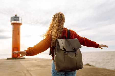 Portrait of woman enjoying a breezy day near a vibrant red lighthouse at sunset. Lifestyle concept.