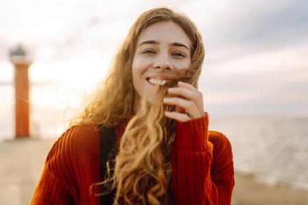 Portrait of woman enjoying a breezy day near a vibrant red lighthouse at sunset. Lifestyle concept.の写真素材