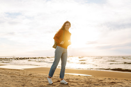 As she walked along the beach, the woman tourist adjusted her backpack, taking in the salty sea airの写真素材