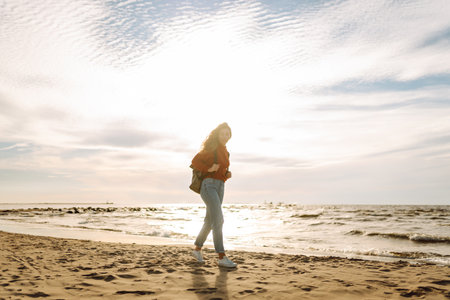 As she walked along the beach, the woman tourist adjusted her backpack, taking in the salty sea airの写真素材