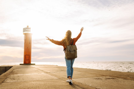 Portrait of woman enjoying a breezy day near a vibrant red lighthouse at sunset. Lifestyle concept.の写真素材