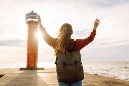 Portrait of woman enjoying a breezy day near a vibrant red lighthouse at sunset. Lifestyle concept.の写真素材